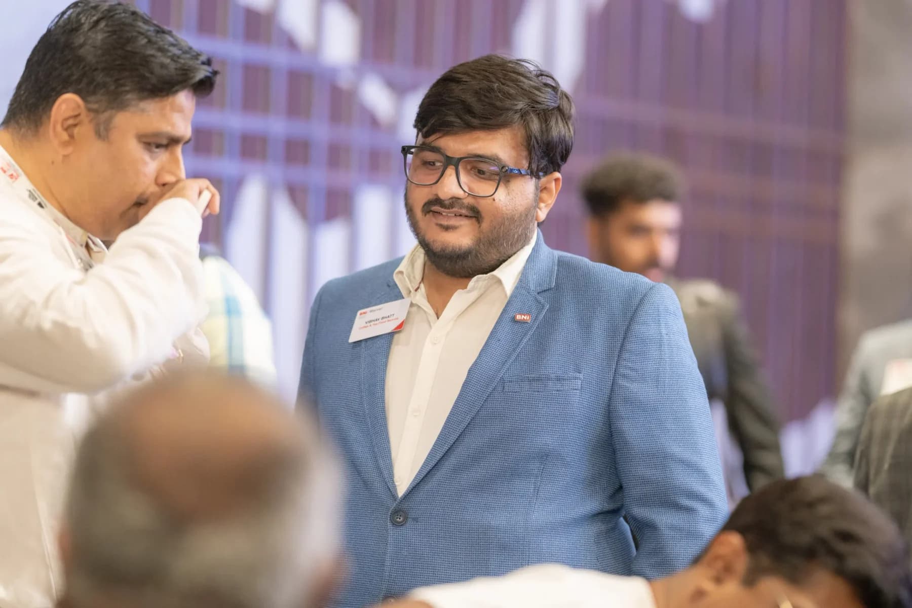 A Travel Nexus member in a blue jacket wearing a BNI name badge, in conversation on the meeting floor