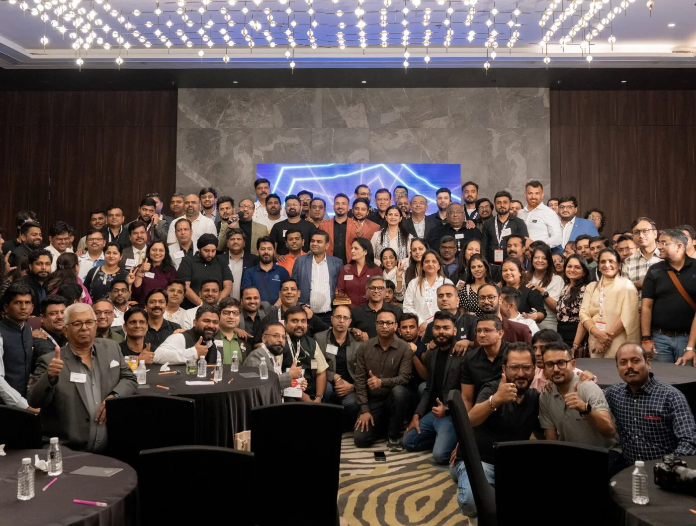 Around two hundred Travel Nexus members gathered for a group photograph in a ballroom beneath a large suspended light installation